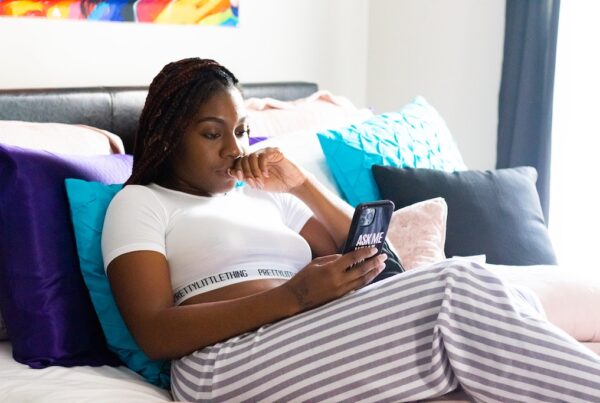 Black woman on iPhone while relaxing in bed.