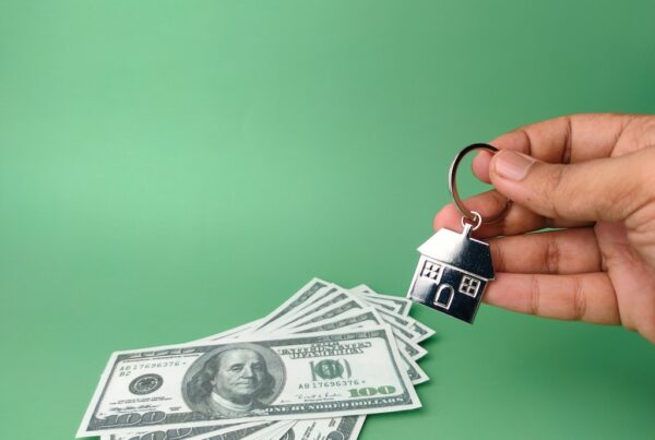Black man holding keyring with a house over a stack of cash.