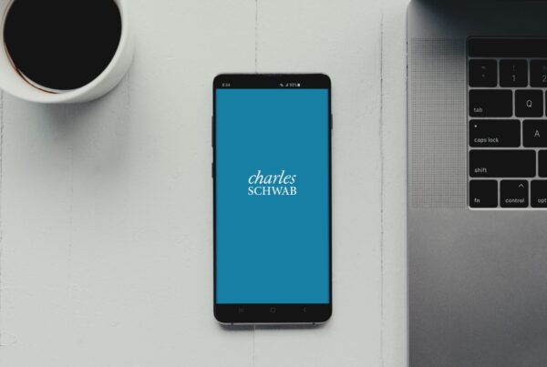 Phone on table near laptop and coffee with Charles Schwab logo on screen.