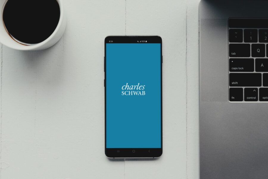 Phone on table near laptop and coffee with Charles Schwab logo on screen.