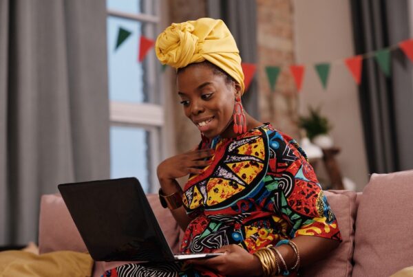 Black woman on couch smiling at laptop.
