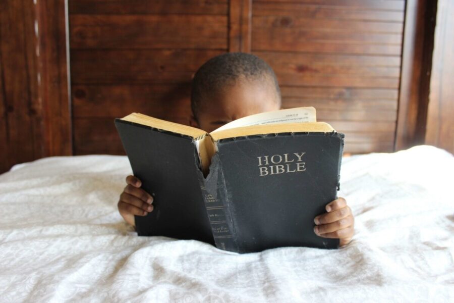a black boy lying in bed, reading a bible | Slavery Impacted Black Investors