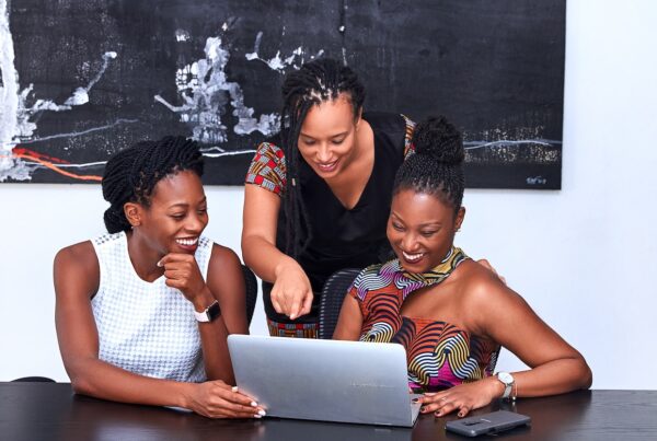 Three black women smiling at a computer on a table | Robinhood Brokerage