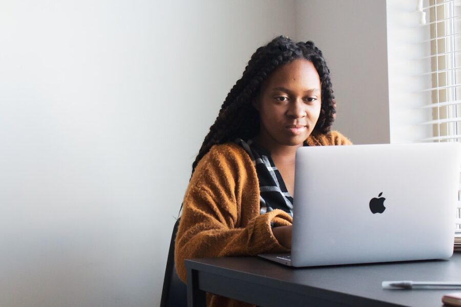 Black woman on Apple Mac laptop at a kitchen table - Investing in Apple Stock