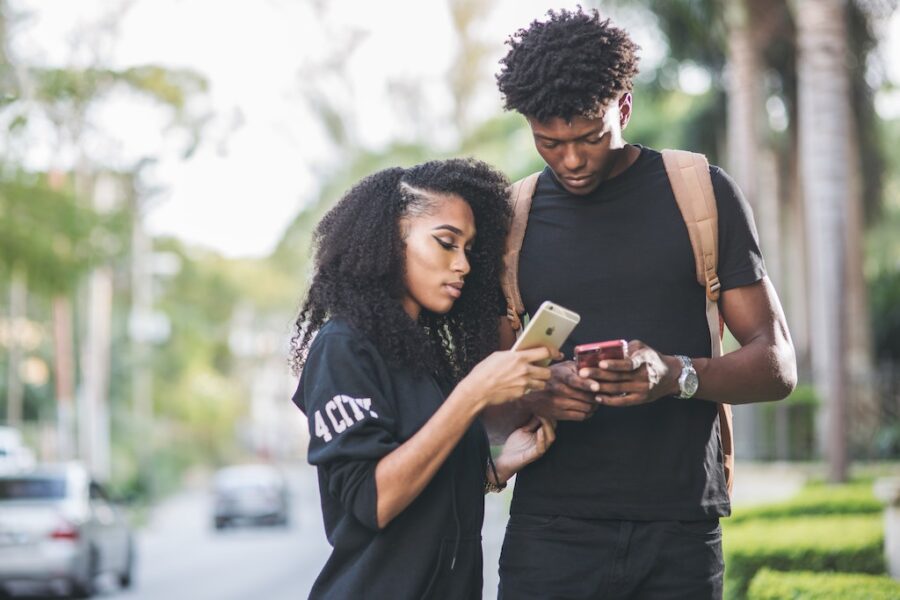 Black woman and black man looking at their phones outside - How Does Inflation Affect Investments