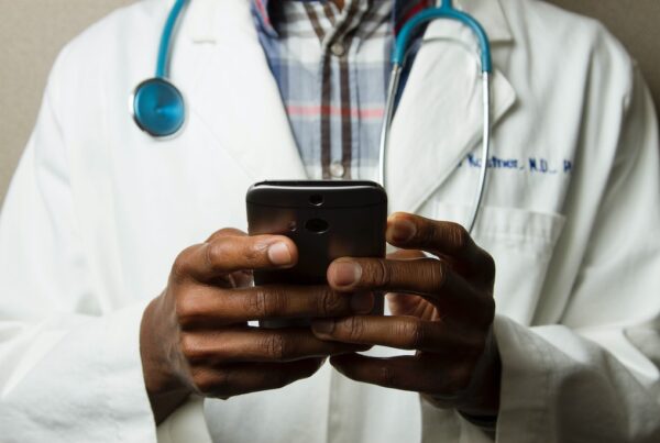 Black doctor in white overcoat with stethoscope reading a smartphone - Make a Healthy Investment with UnitedHealth Group