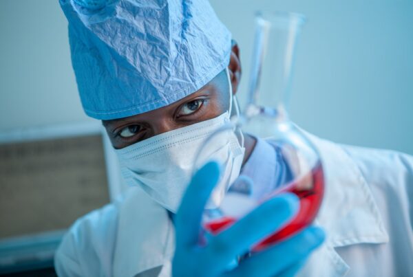 Black scientist holding red liquid in a beaker.